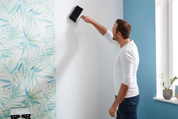 Person bringt mit einer Bürste Kleister an eine Wand an